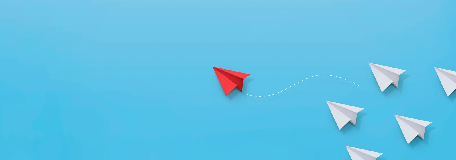 A red paper airplane breaking away from the white ones, tracing its own path.
